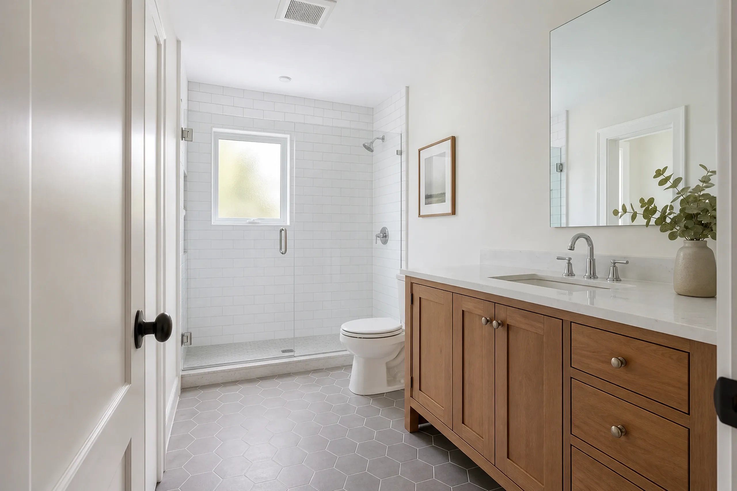 Bathroom remodeling: bathroom with a glass-door shower in white subway tile, a wood vanity with a pale stone top, gray hexagon floor tile and a frosted window