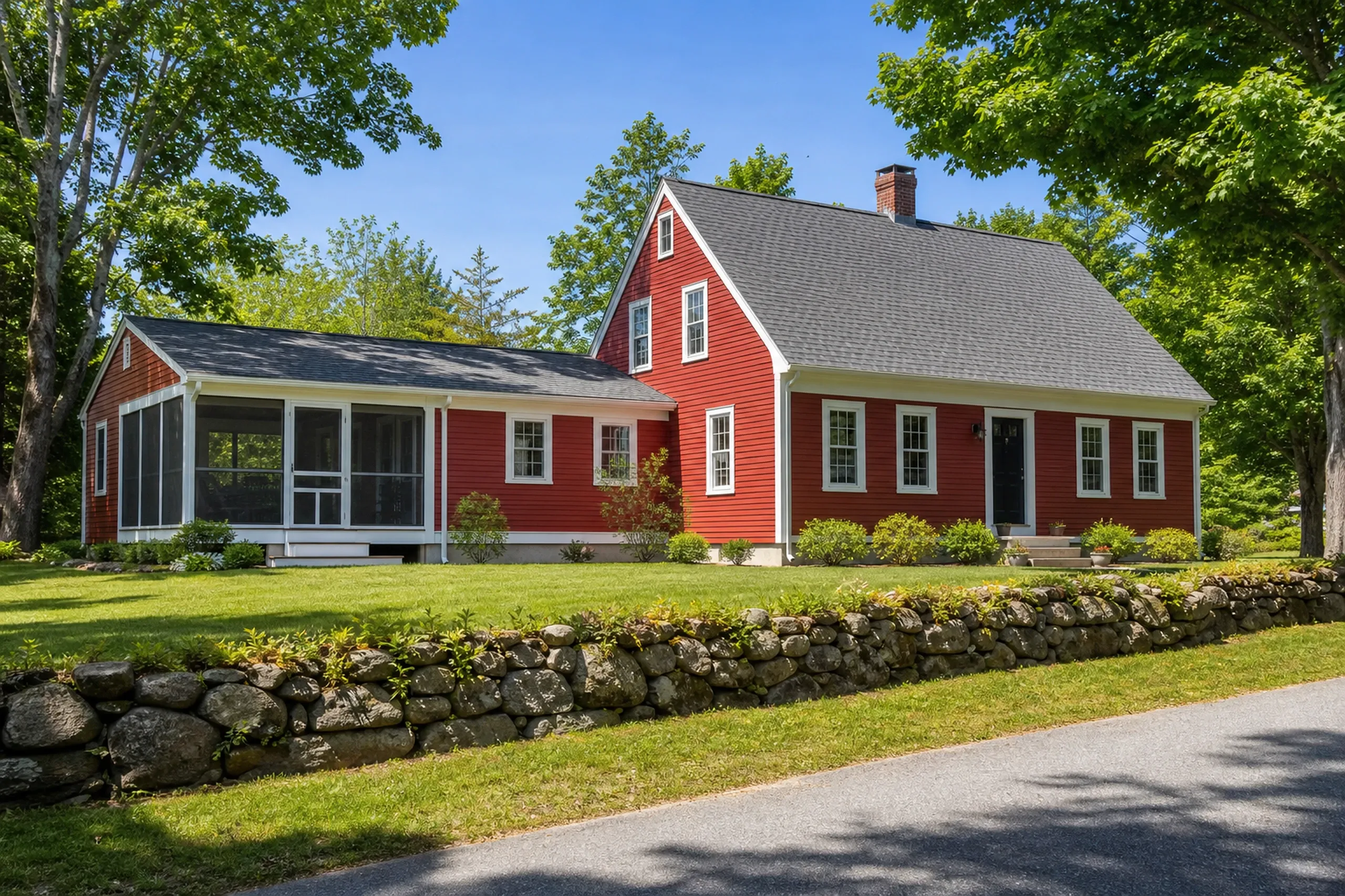 Home additions: red house with white trim, a brick chimney and a screened porch addition at left, sitting behind a fieldstone wall and a paved road